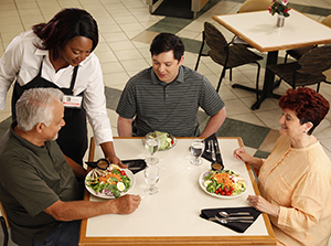 Waitress serving healthy food to two men and a woman in restaurant.
