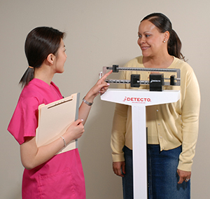 Woman standing on scale at doctor's office, smiling, happy.