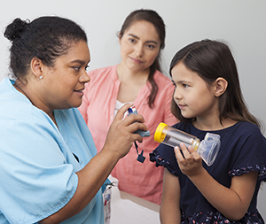 Healthcare provider showing woman and child a metered-dose inhaler with spacer and mask.