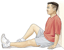 Man sitting on floor with back against wall. One knee is bent with foot flat on floor. One leg is stretched out straight on floor.