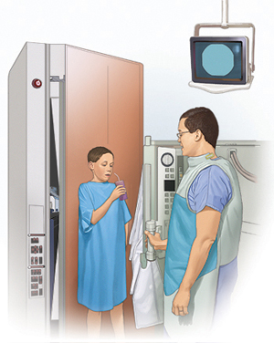 Boy in hospital gown standing in front of X-ray machine drinking contrast liquid. Healthcare provider is standing nearby.