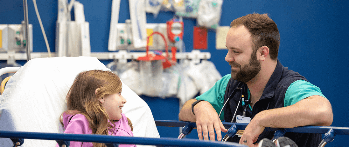 A BayCare physician smiles at a young female patient who is smiling in a hospital bed.