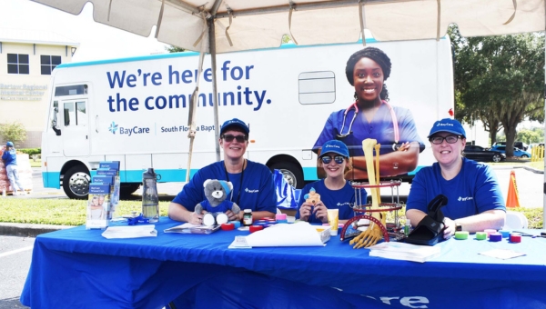 A group of people sitting at a booth outside of a BayCare facility for a community event.