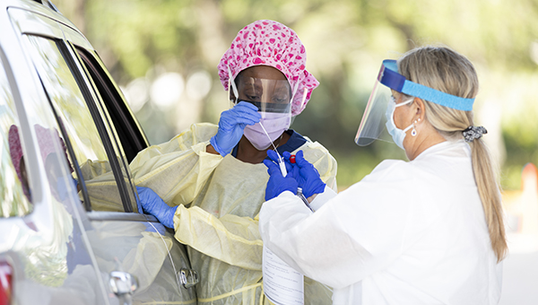 Two BayCare team members, who are wearing personal protective equipment, perform a coronavirus test on someone at a drive-thru testing location.