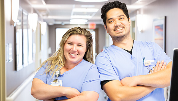 Two smiling BayCare team members, a woman and a man, are standing in the hallway of a BayCare facility.