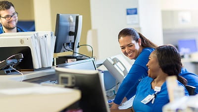 Two female nurses and a male nurse are talking at the nurses station at a BayCare facility.
