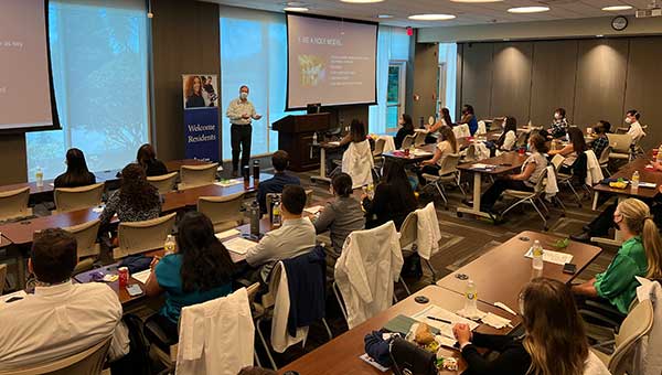 a seminar with a speaker and a large audience sitting at desks