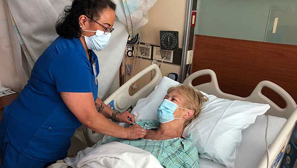 female care professional in baycare blue scrubs helping a female patient in hospital bed