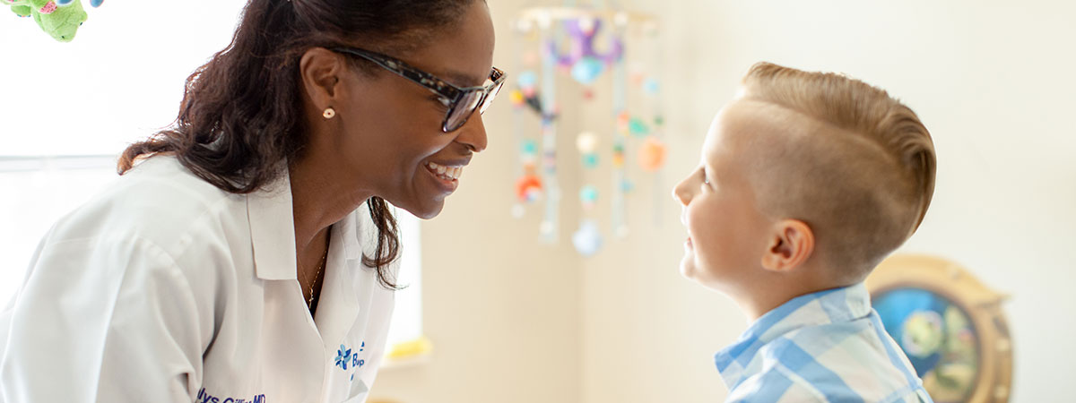 female physician in lab coat smiling and speaking with a young boy