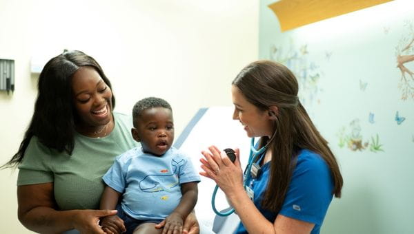 A nurse interacting with a young patient and the mother is holding the young patient