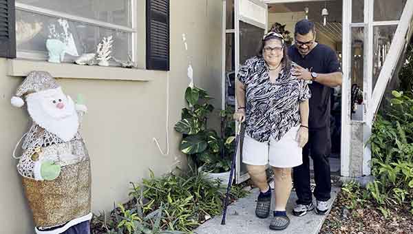 A woman walking out of her home after knee surgery with assistance from a BayCare physical therapist.