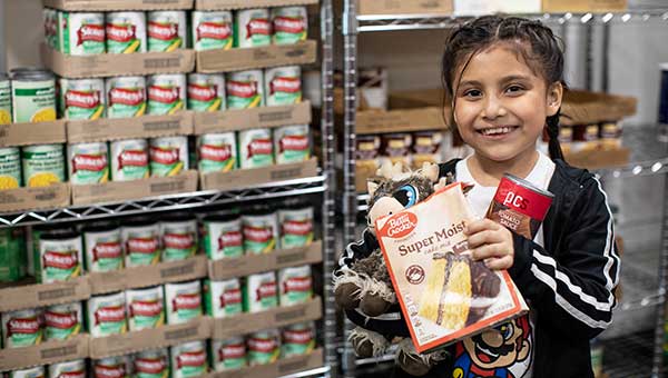 happy young girl holding food next to shelves at food pantry