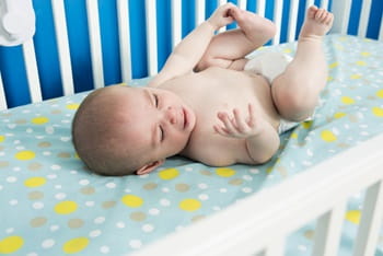 A cute one month old newborn is laying on their back in their crib crying