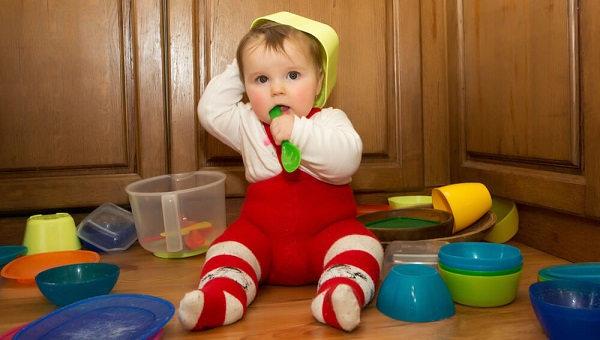 Adorable baby girl pulling pots and pans and other dishes out of a kitchen cupboard