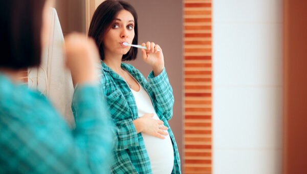 pregnant woman looking in mirror while brushing teeth