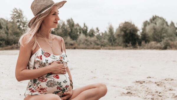 pregnant woman on beach with hat and sundress