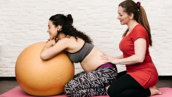a pregnant woman leaning over an exercise ball