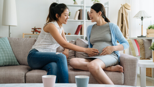 a pregnant woman sitting on the couch with her friend