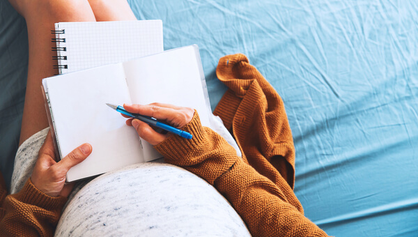 a pregnant woman writing in her notebook