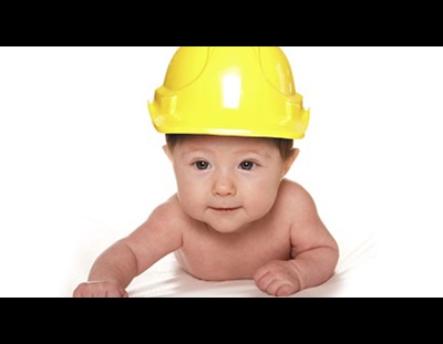 A baby is wearing a little yellow hard hat.