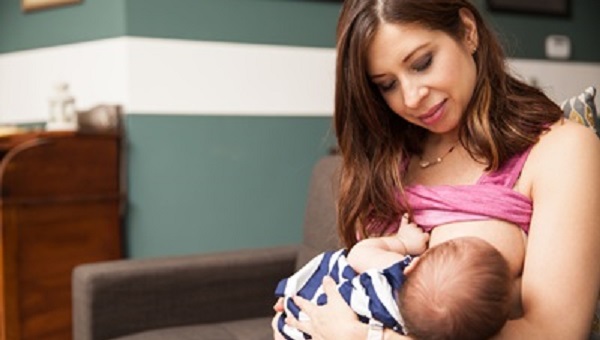 beautiful mother breastfeeding her newborn while sitting on a couch at home