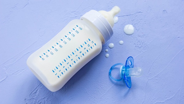 Bottle of milk for a newborn and a blue silicone soother at blue vintage background