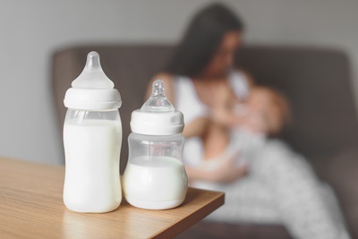 Bottles with breast milk and mother holding baby and breastfeeding