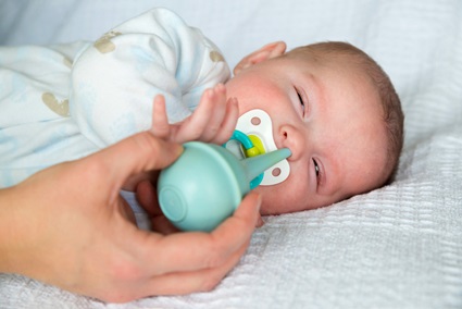 Mother using bulb syringe to clean unhappy infant baby's nose