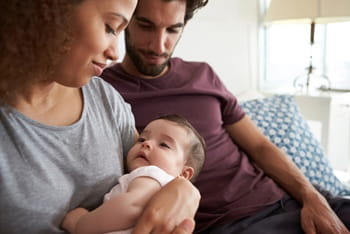 Parents sitting on sofa cuddling baby daughter at home