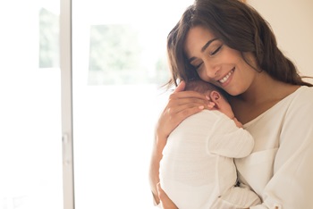 A young mother is cradling her newborn baby in her arms.
