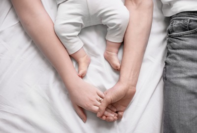 Young parents holding hands together with little baby lying on bed