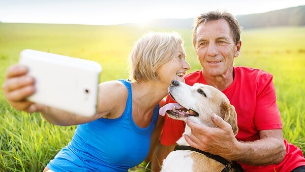 husband and and wife taking photo with dog in field