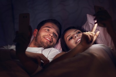 A young couple checks their cellphones in bed before going to sleep.