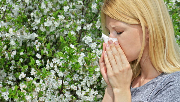 A woman using a tissue near a garden of flowers