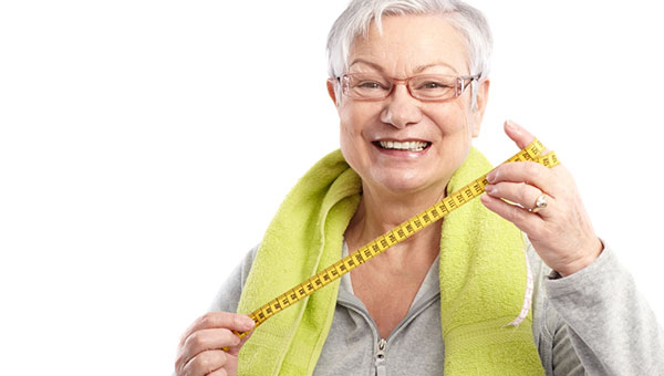 A senior woman is holding a tape measure after a workout session.