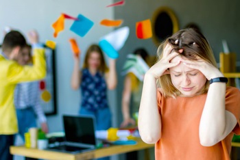 women holding her head in chaotic office environment