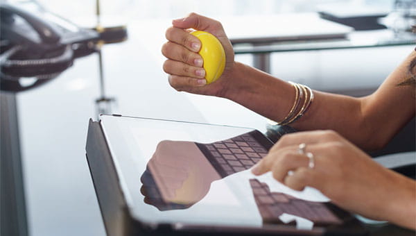 A woman is squeezing a stress ball while sitting in front of her computer.