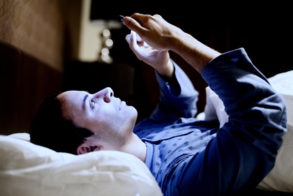 A man is checking his cellphone while in bed.