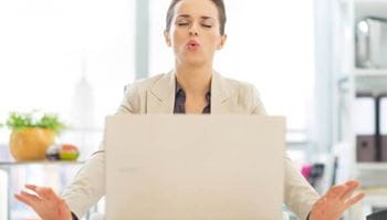 A woman does breathing exercises while sitting in front of her laptop computer.