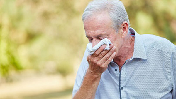 A senior man is wiping his nose with a handkerchief.