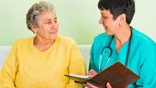 A woman doctor takes notes while talking with a senior woman patient.