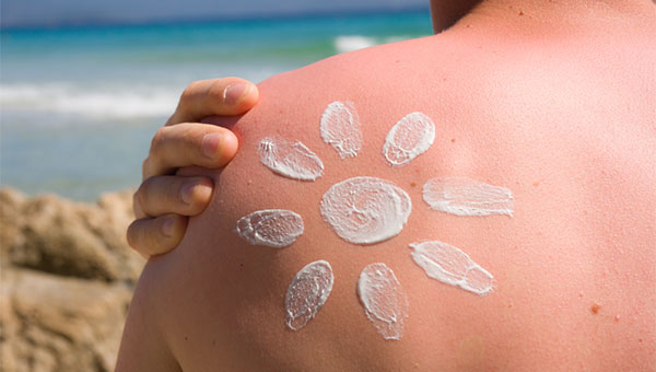 A man puts sunscreen on his shoulder at the beach.