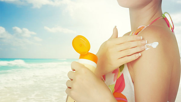 A woman puts sunscreen on her shoulder at the beach.