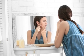 girl in a blue tank top looking at her face in a mirror
