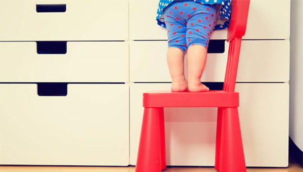 A toddler is standing on a step stool to reach something on a counter