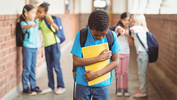 A boy walks through his school hallway while his classmates point at him and tease him.