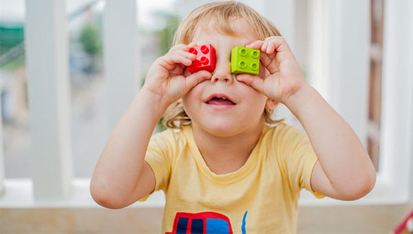 A young boy holding up two Legos over his eyes