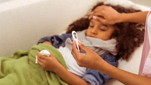 A mother has her hand on her daughter's forehead while checking her temperature on a thermometer