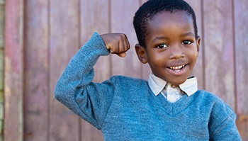 A young boy smiles while flexing the muscles in his right arm.
