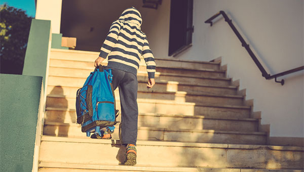 A child carries a heavy backpack up a flight of stairs at school.